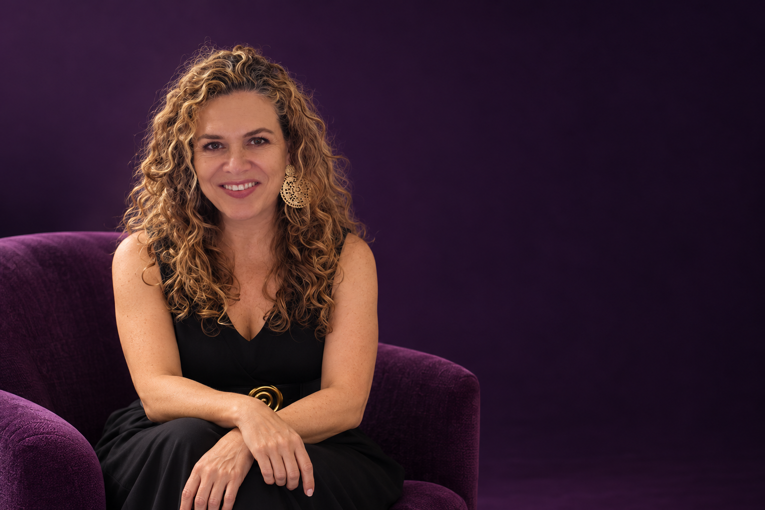 Sandra Echeverri sonriendo en un sofá morado, con vestido negro y el fondo original de su fotografía